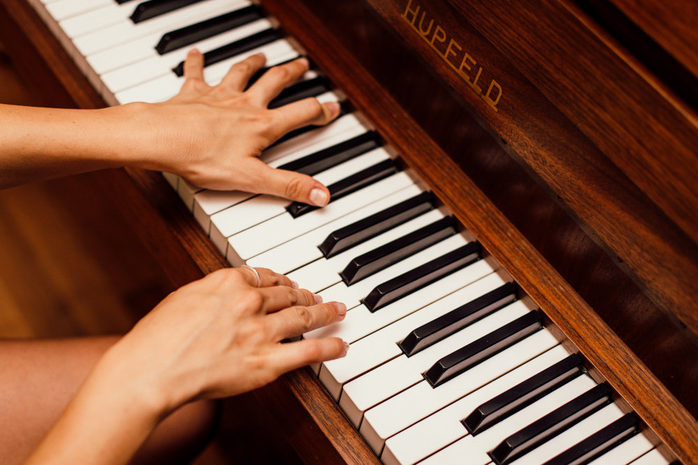 fotografia przedstawia klawisze pianina oraz dłonie osoby na nim grającej
